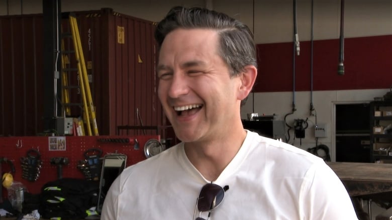 Pierre Poilievre, smiling, with a wall full of tools behind him.