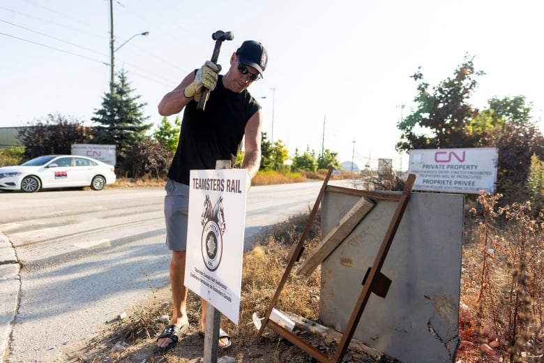 A man hammering a sign into the ground that reads: Teamsters Rail, outside a CN Rail yard in Vaughan, Ont.