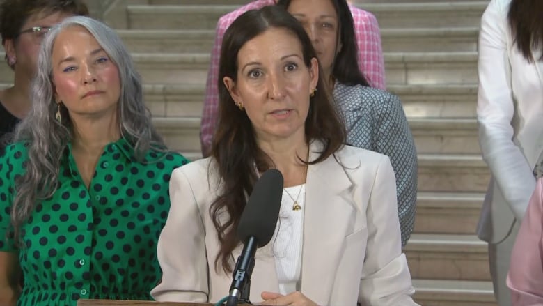 A woman with long hair speaks at a podium 