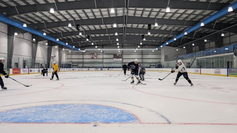 Hockey players skate on a large indoor rink.