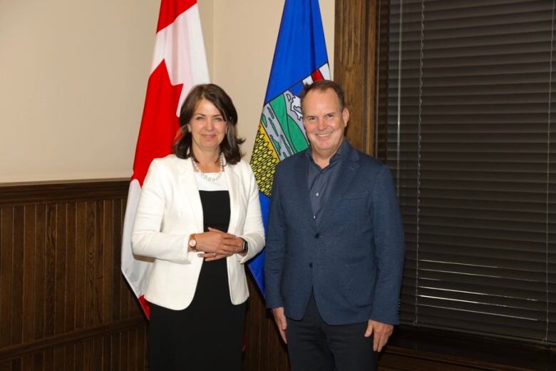 A woman and a man stand in front of two flags.