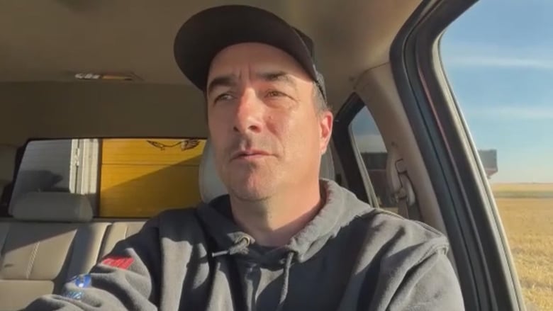 A man sits in a truck in a field.