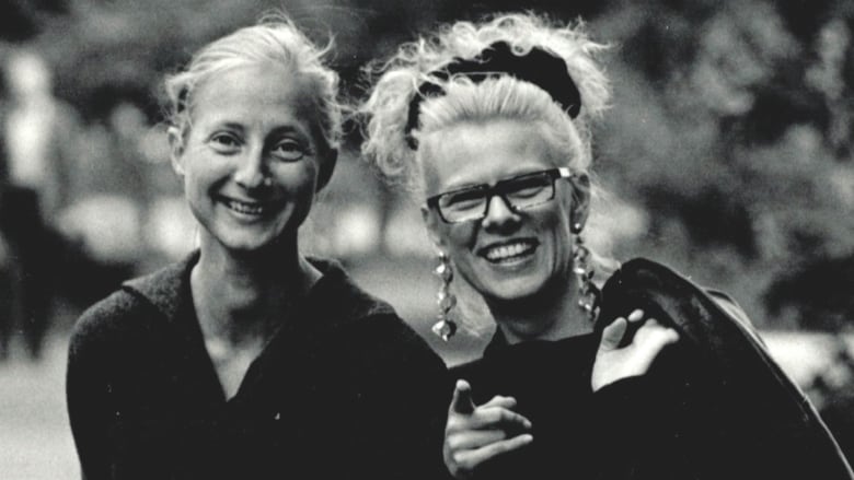 A black and white photo of two women smiling and posing in a park. 