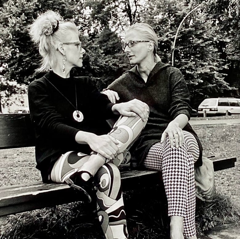 A black-and-white photo of two women sitting on a park bench.