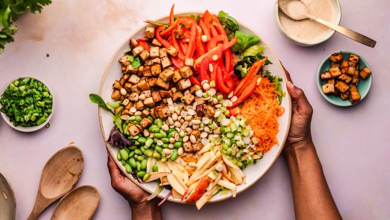 Chopped salad filled with tofu. red peppers, grated carrots, diced green onion, raw peanut halves and apple slices, topped with sesame dressing