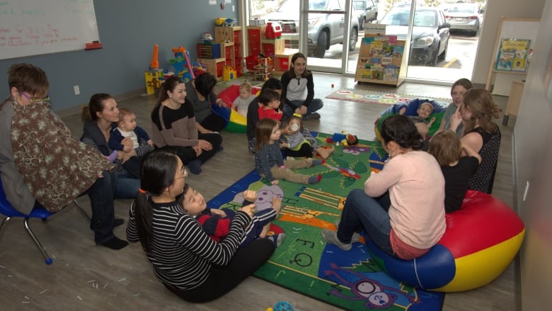 A group of parents and kids sit on a carpet in a room.