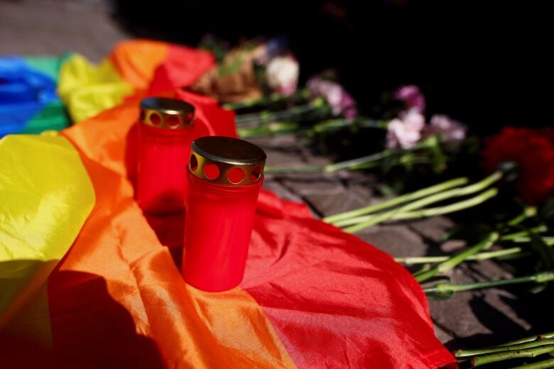 A rainbow flag and candles are arranged on the ground.