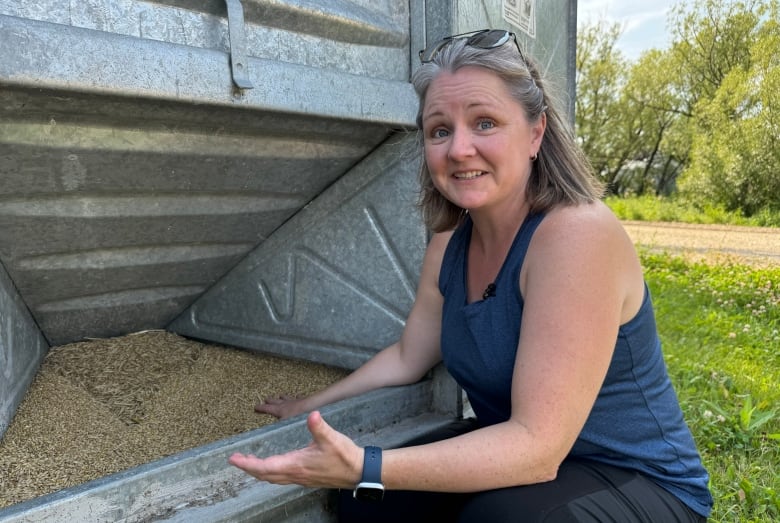 A woman kneeling outdoors in front of some grain in a silo.