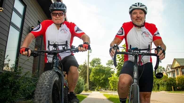 Two men sit on bikes.