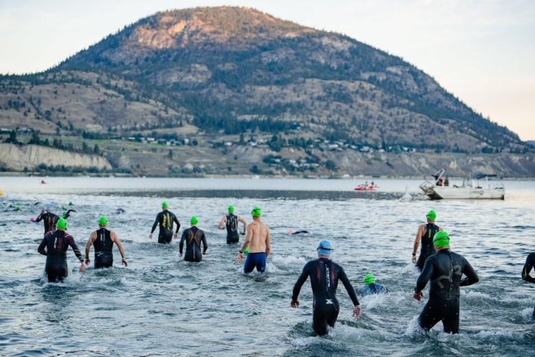 Swimmers in a river with a hill looming large in the background.