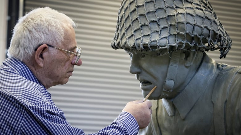 A man makes adjustments to the face of a large statue.