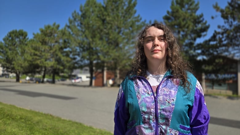 A woman stands in front of trees. 