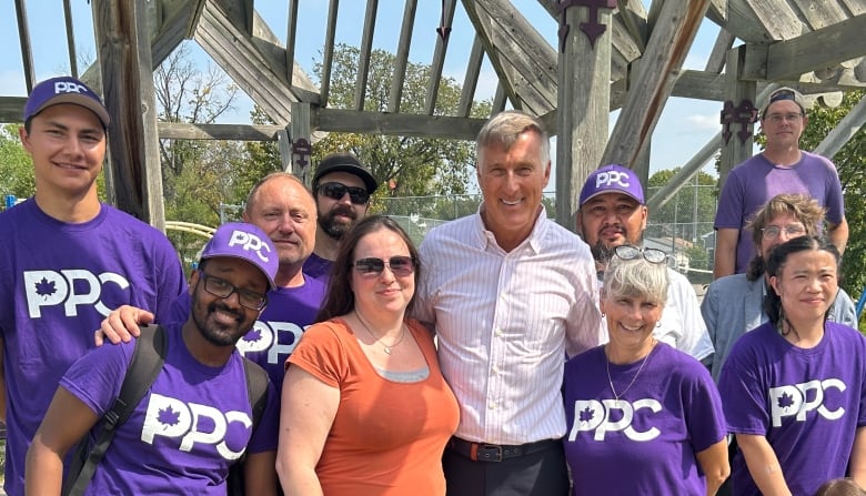 A man and a woman surrounded by a handful of people wearing purple shirts and hats with the PPC logo.