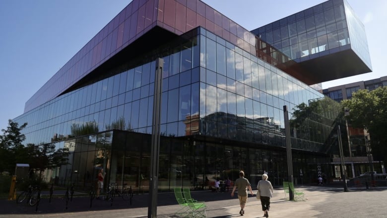 Two people are walking towards a big glass building on a sunny day.