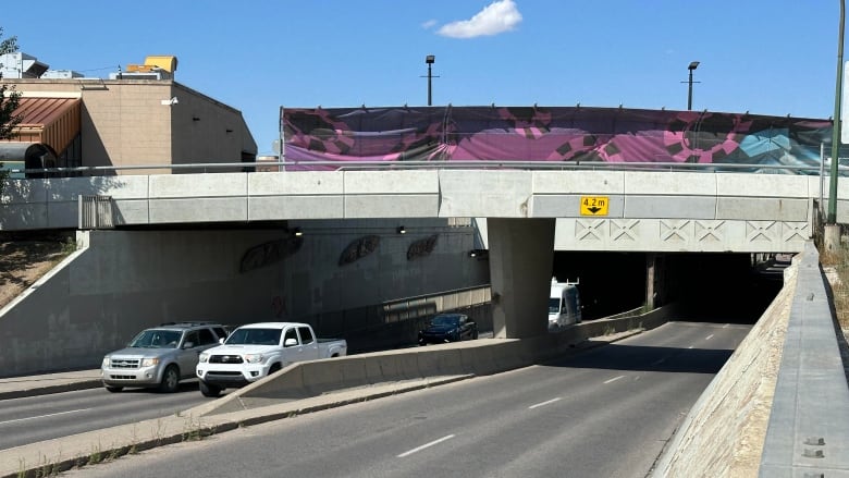 Vehicles pass through a concrete underpass during the day.