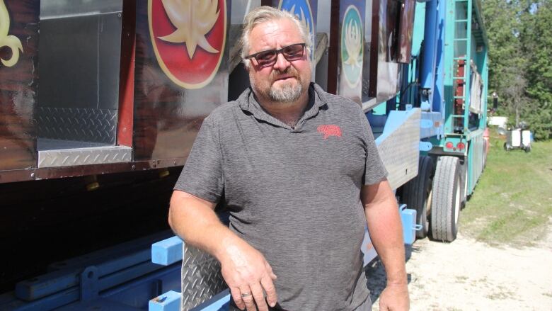 A man in a black t-shirt stands next to an amusement ride in a semi-trailer.