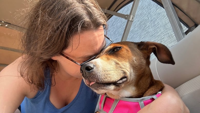 Dark-haired woman presses her face to the face of a short-haired brown dog. 