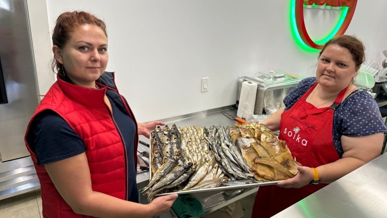 Two women hold a large tray of fish. 