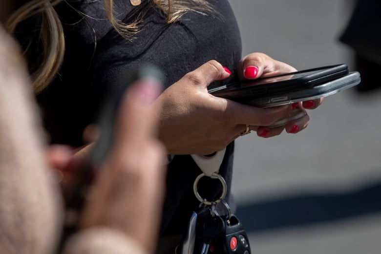 A hand holds a cellphone with both thumbs pressed on the screen as car keys dangle from their fingers.