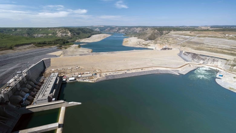 An aerial view of a large dam on a sunny day, with clean water on either side.