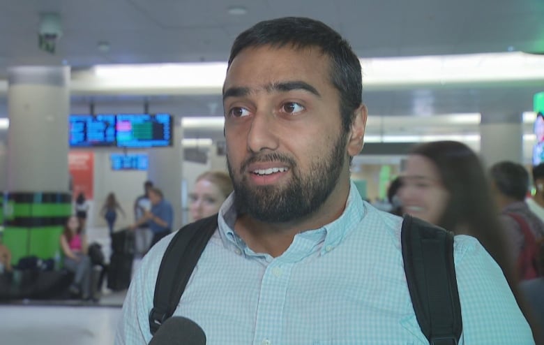 The photo shows Bilal Malik, a young adult, standing at the GO Train station. He is wearing a blue buttoned up shirt and has a backpack on his shoulders 