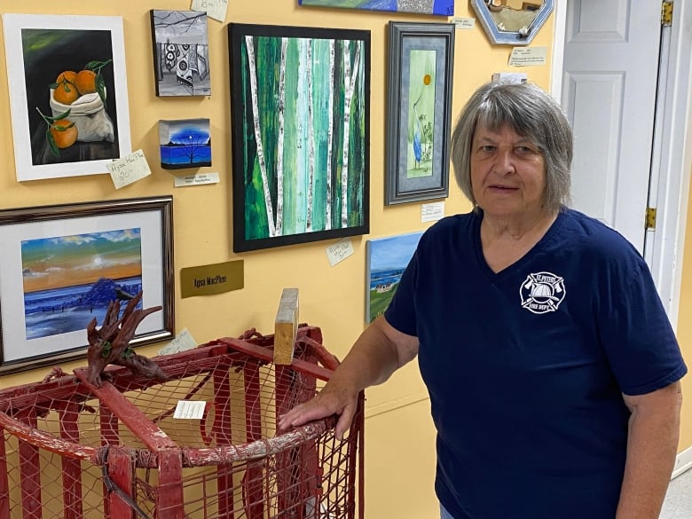 Woman stands next to wall with framed pictures. She rents her hand on a red lobster trap.