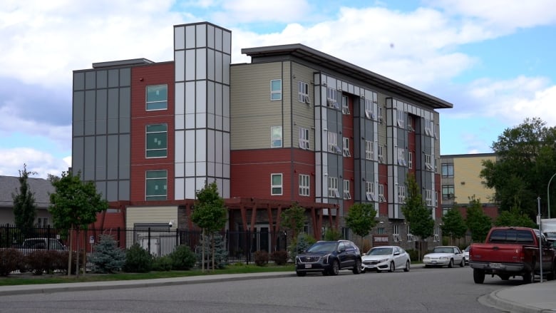 A photo of a three-storey red and tan building fronted by windows and small balconies with a white tower on the side and more windows.