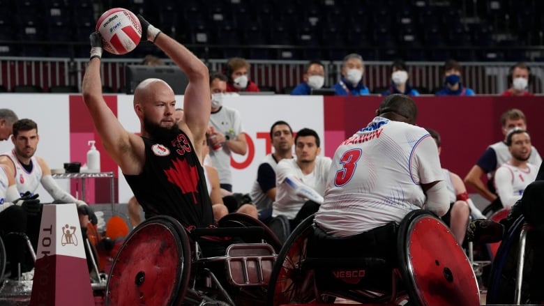 A man in a wheelchair is pictured holding a ball above his head with another man with his back to the camera opposing him.