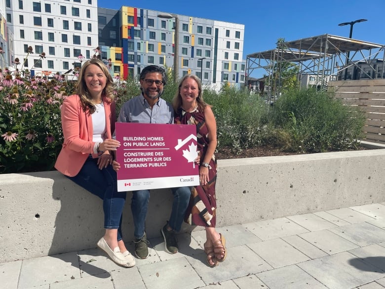 Three people smiling and holding a sign. 