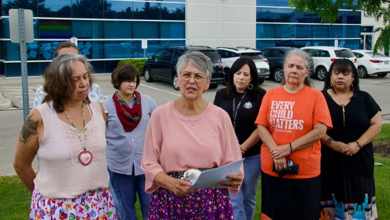 Seven people stand in a group by an outdoor parking lot