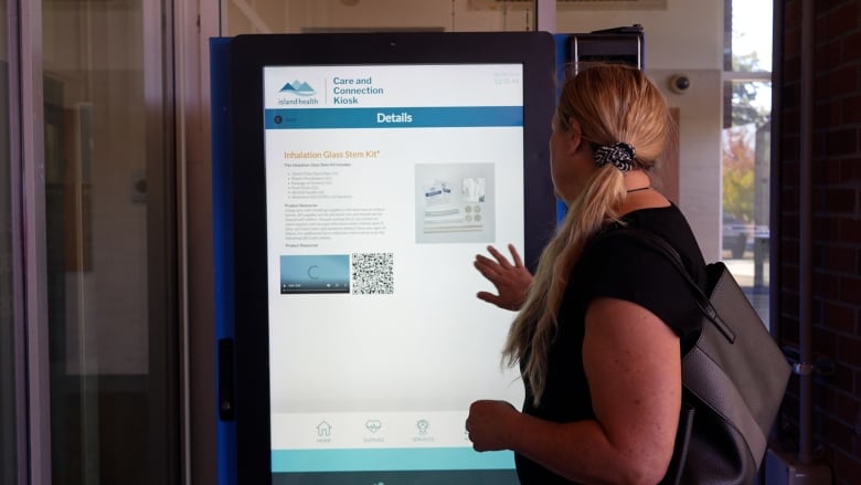 A woman at a vending machine kiosk with her hand on the glass as if to make a selection.