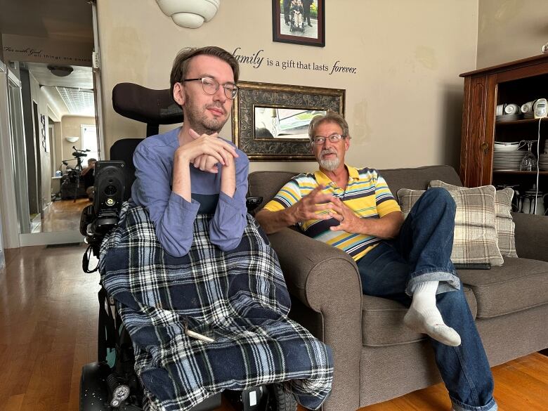 A man in a wheelchair and his father who is seated on a couch.