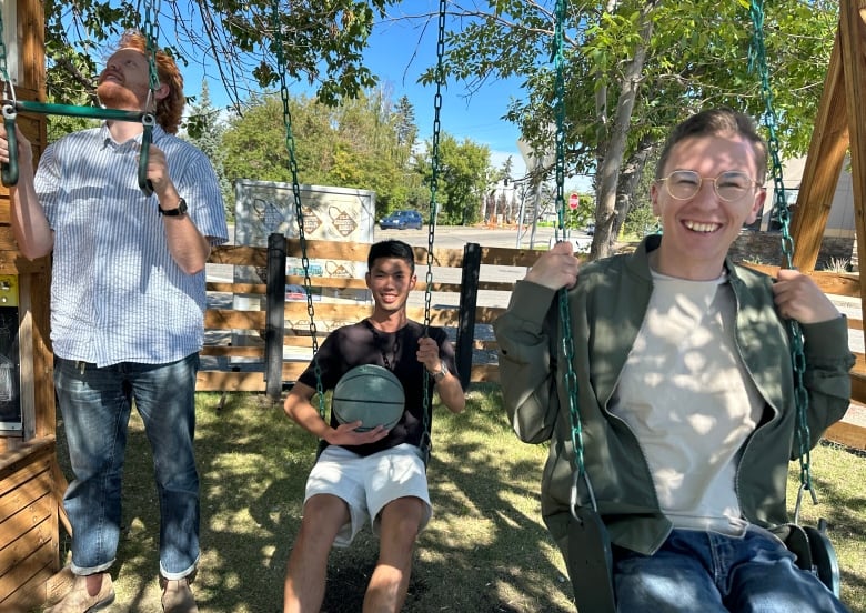 Two men sit of children's swings while a third hangs on to the monkey bars.