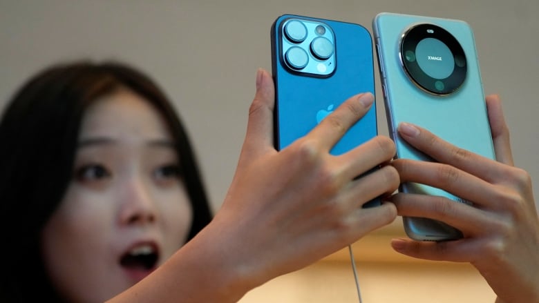 A woman looks excitedly up at two phone she is holding, one in each hand. Her left hand uses her pinky to prop up the phone she is holding. 