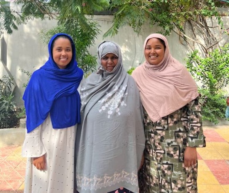 Three women wearing head scarves and long robes stand side by side.