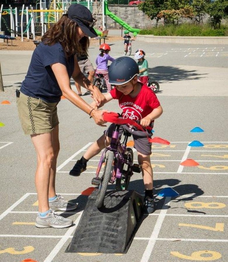 Mom helps boy bike over a small ramp