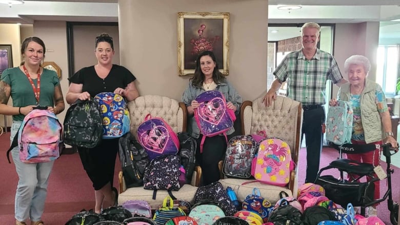 A group of people standing in front of a couple of dozen children's backpacks (with cartoon characters on them) on the floor.