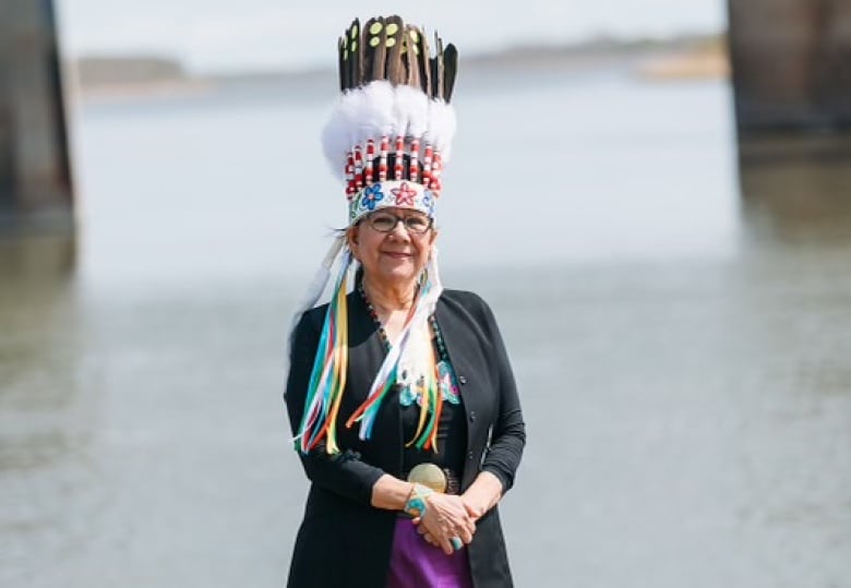 A woman wearing a headdress in front of a body of water posing for a picture.