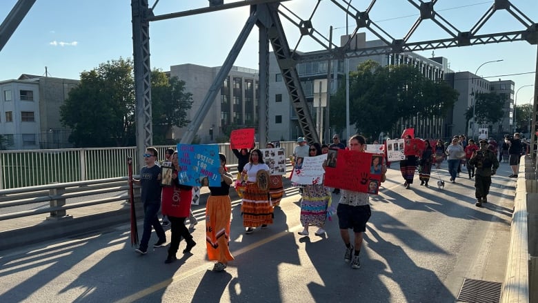 People crossing a bridge while holding signs