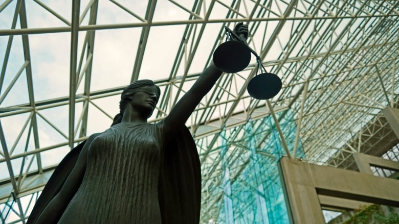 A statue of a blind goddess holding the scales of justice in a large windowed atrium.