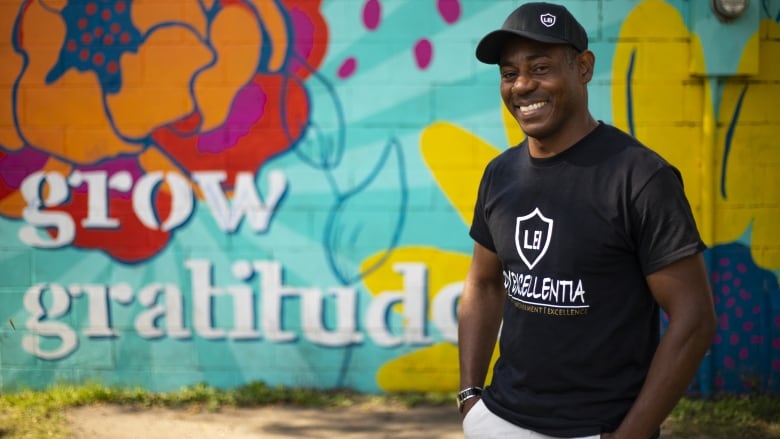 A man stands in front of a mural that says grow gratitude.