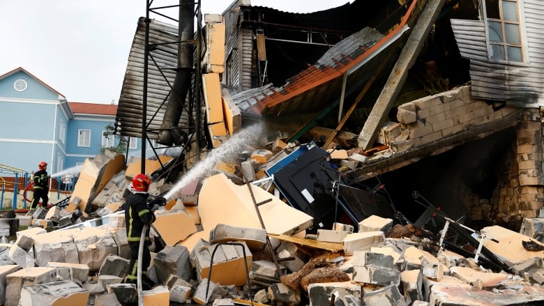 Firefighters spray water on a charred and destroyed building,