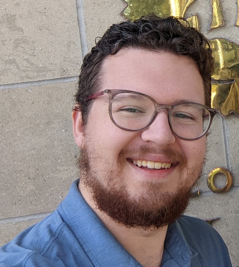 A portrait of a person with glasses, a beards and a button-up shirt. 