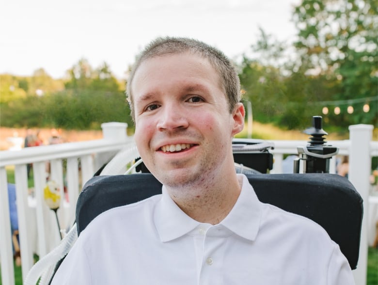 A portrait of a person in a dress shirt seated in a wheelchair. 