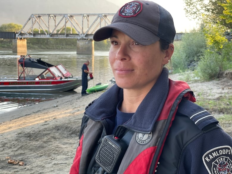 A woman wearing a fire captain uniform stands in front of a river and rescue boat