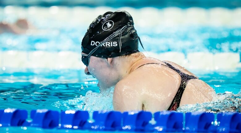 A woman popping up out of the water. She wears a swim cap that says 