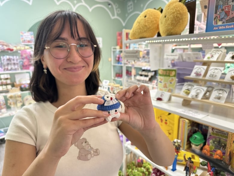 A woman holds a small crocheted figurine on a keychain.