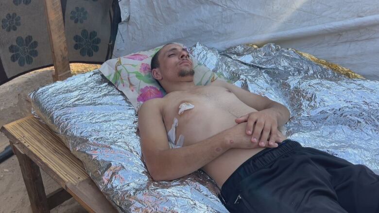 A man lays shirtless with a bullet wound in his chest