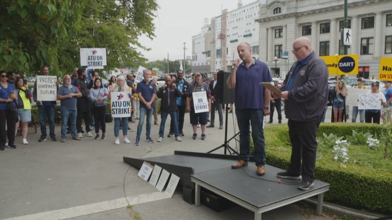 A man speaks at a rally, surrounded by hundreds of people.