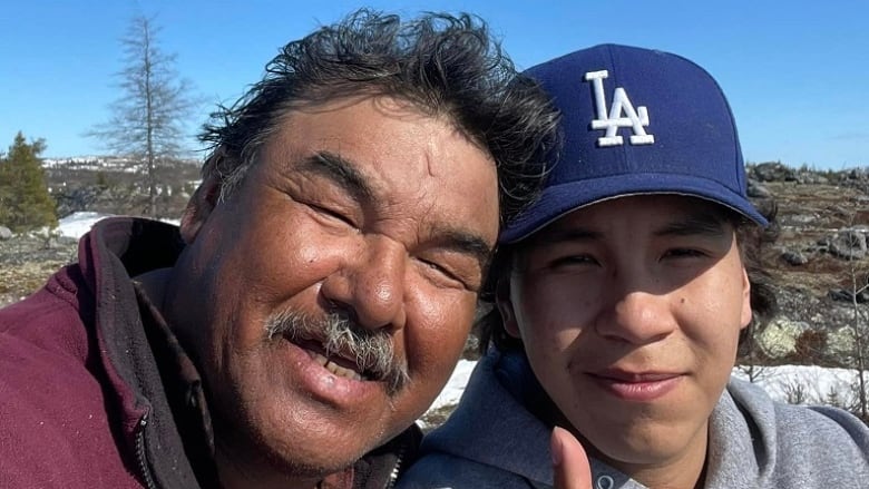 A Cree elder and his grandson smile at the camera on the land